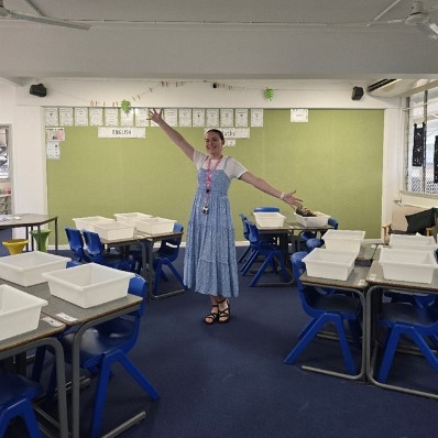Angela stands in a classroom with her arms out wide.