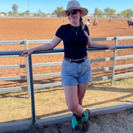 Angela stands in front of a fence at the rodeo.