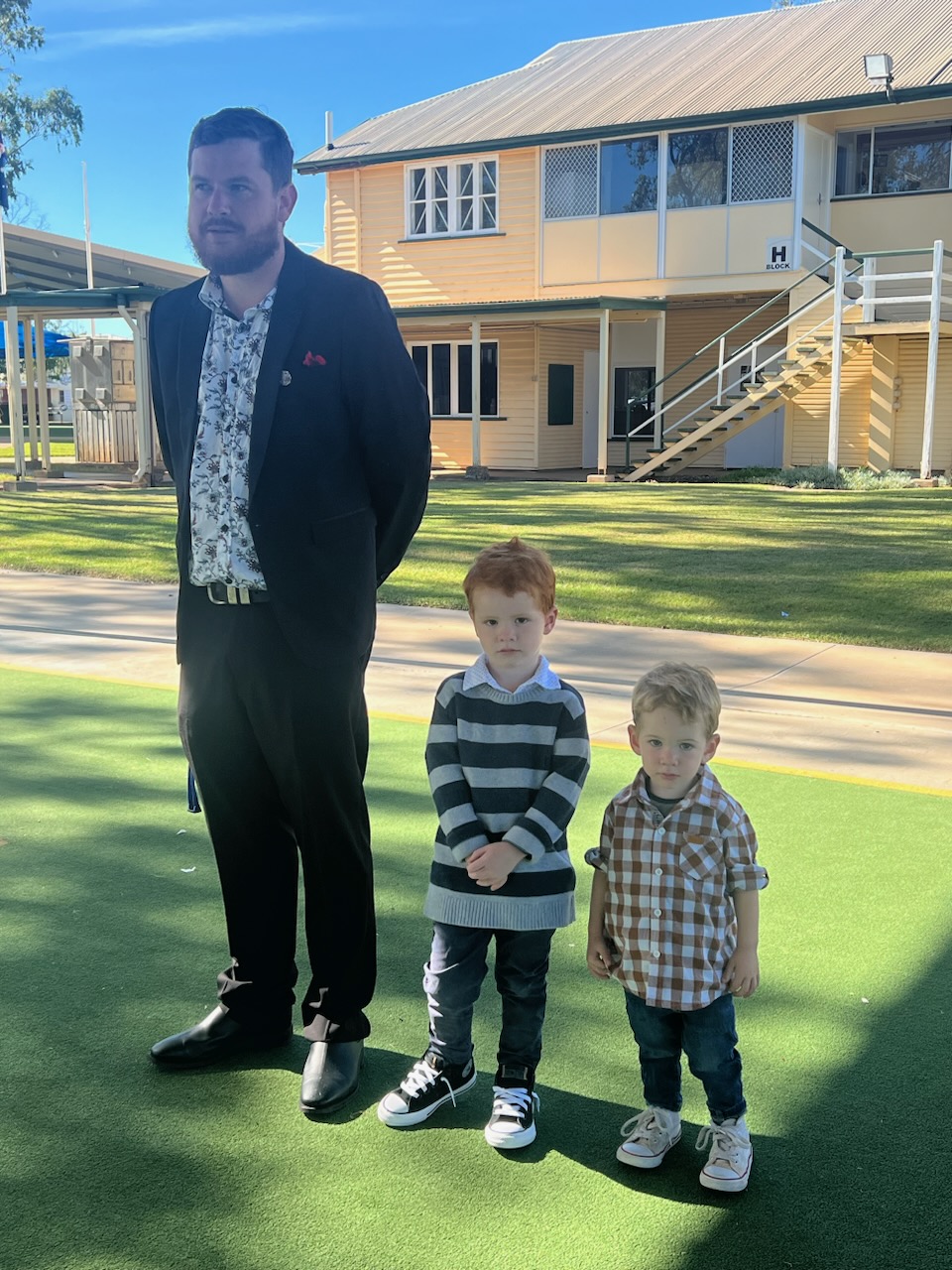 Photo of Nathan and his two children standing in front of a school building.