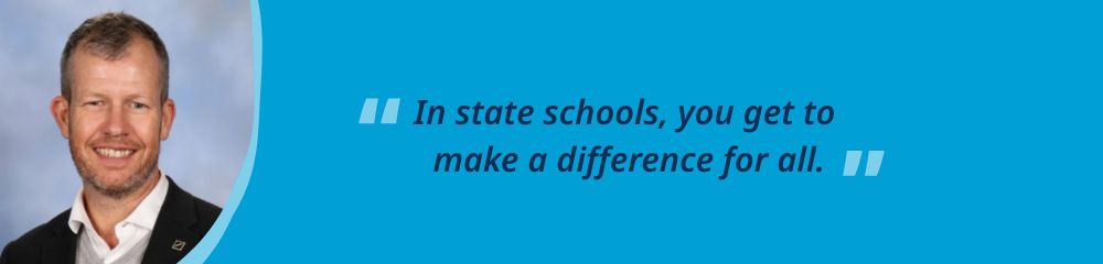Photo of a male teacher, Travis, smiling at the camera, tan pale skin with dark brown short hair and a beard. He is wearing a white shirt and black jacket. Blue background and white text that says 'In state schools, you get to make a difference for all.'