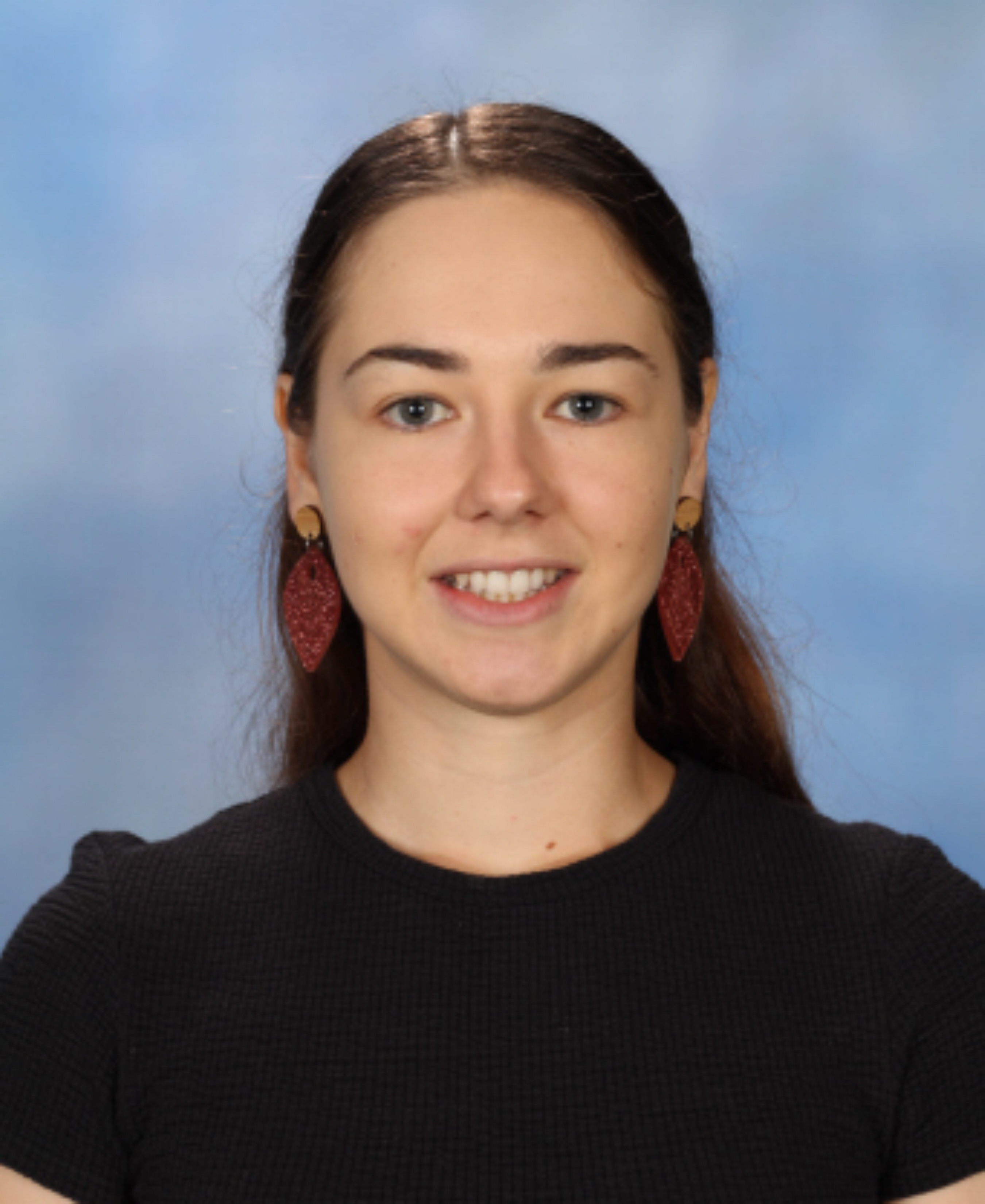 Photo of female teacher, Jess. She has pale skin and long dark brown hair. She smiles at the camera and wears a black top.
