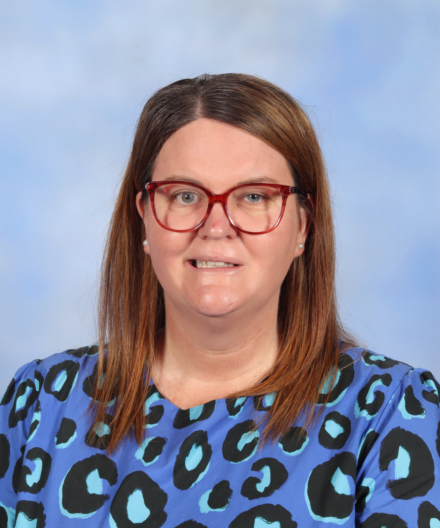 Photo of female teacher, Lisa, with shoulder-length brown hair and pale skin. She smiles at the camera and wears a blue top.