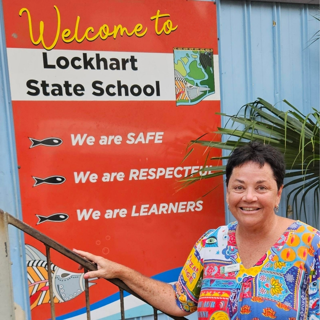 Photo of female teacher standing in front of Lockhart State School sign that says 