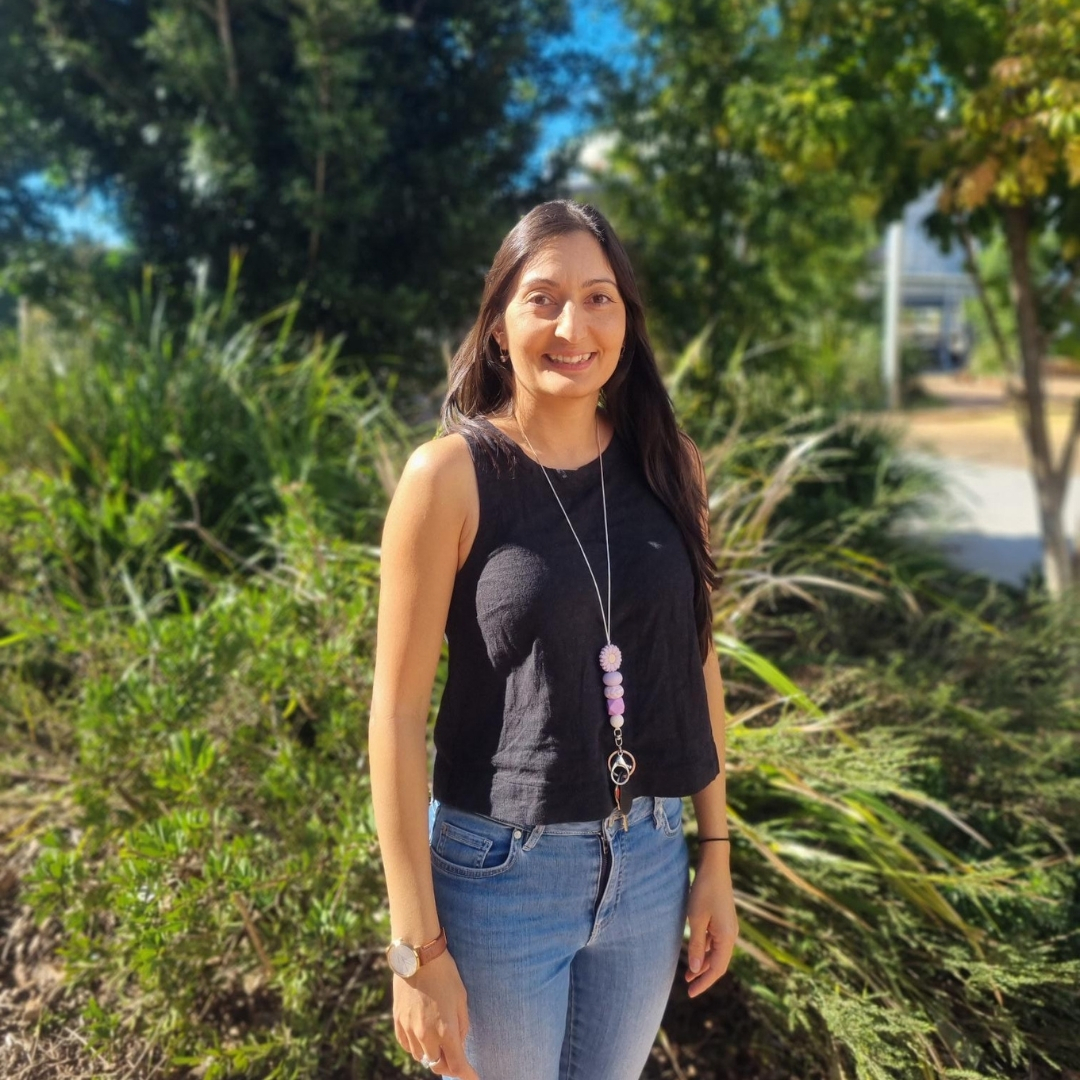 Photo of female teacher smiling in front of camera and standing in front of trees.