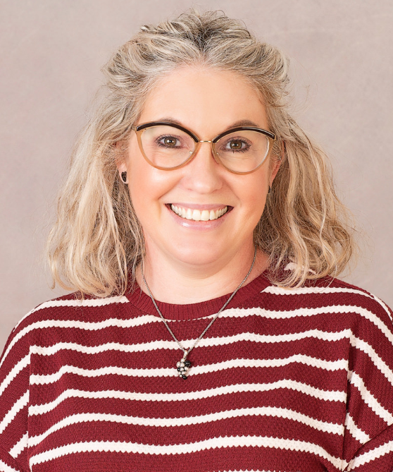 A photo of Principal, Rachel, smiling at the camera. She has glasses, blonde hair and wears a red and white striped top.