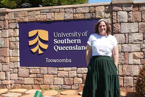 Teacher standing in front of University of Southern Queensland, Toowoomba sign